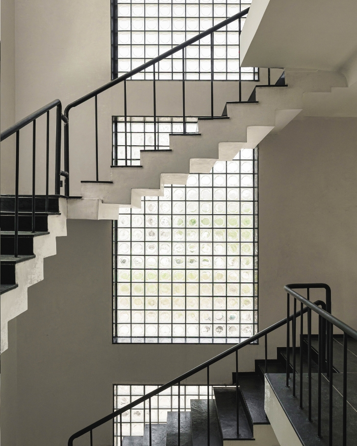 A sculptural staircase with crisp white geometry and a minimalist black railing creates a dramatic play of light, shadow, and movement through the home's vertical core; Photography by Studio Beyond Walls