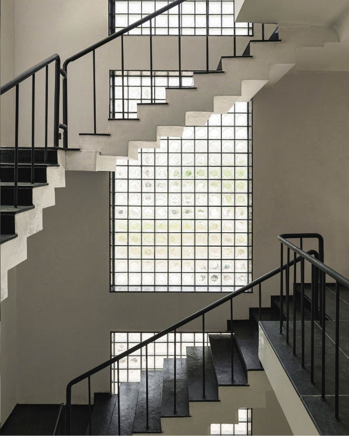 A sculptural staircase with crisp white geometry and a minimalist black railing creates a dramatic play of light, shadow, and movement through the home's vertical core; Photography by Studio Beyond Walls